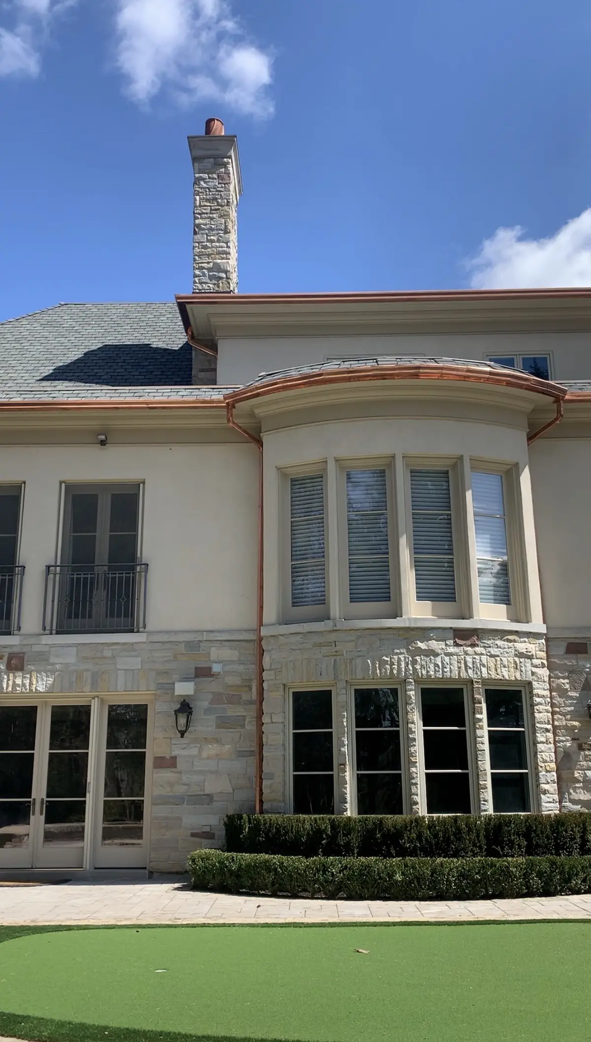 Stone and stucco home with copper roofing over the bay windows