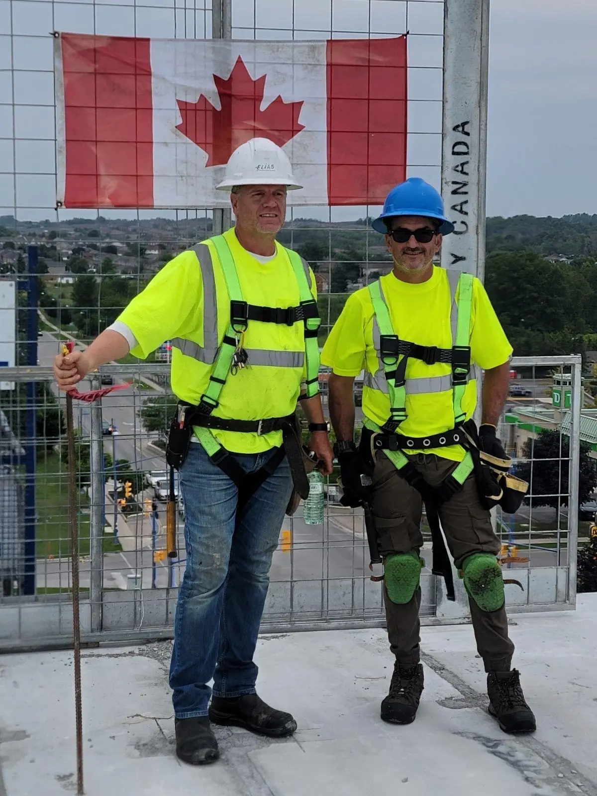 Two Eagle Roofing roofers in safety harnesses and hi-vis vests in front of a Canadian flag