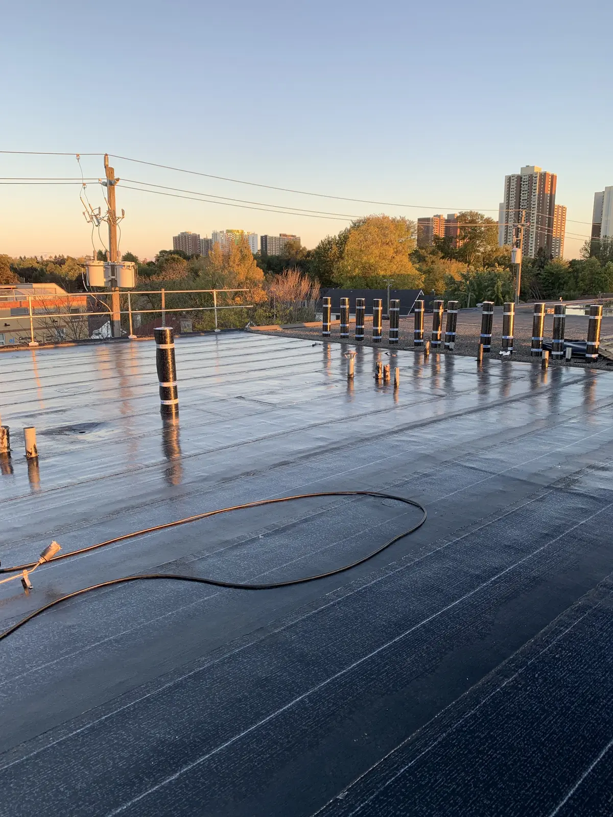 Freshly installed flat roof membrane at sunset, city towers behind