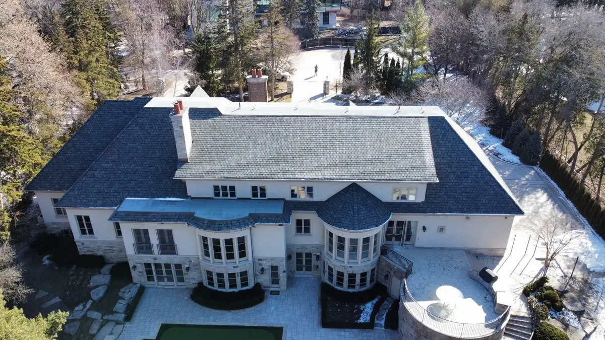 Aerial view of a large estate home with a new dark roof, after a snowfall