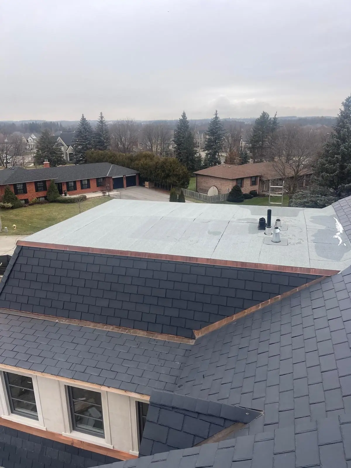 Synthetic slate roof with copper flashing beside a flat roof section