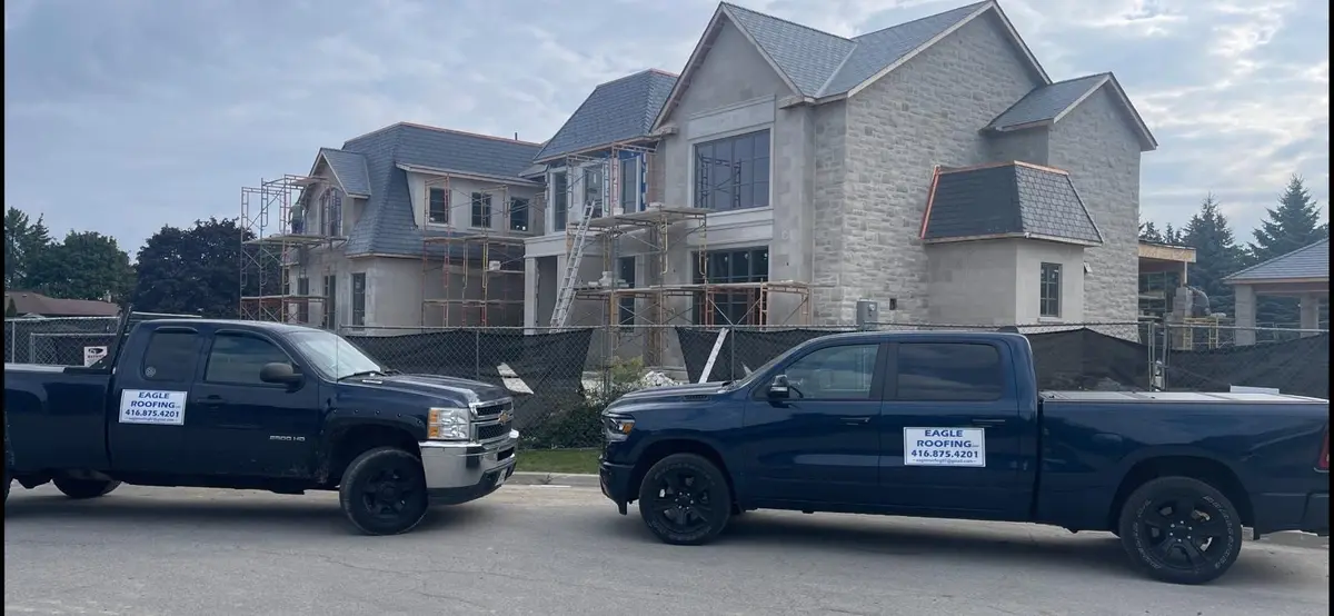 Two Eagle Roofing pickup trucks parked outside a large home under construction